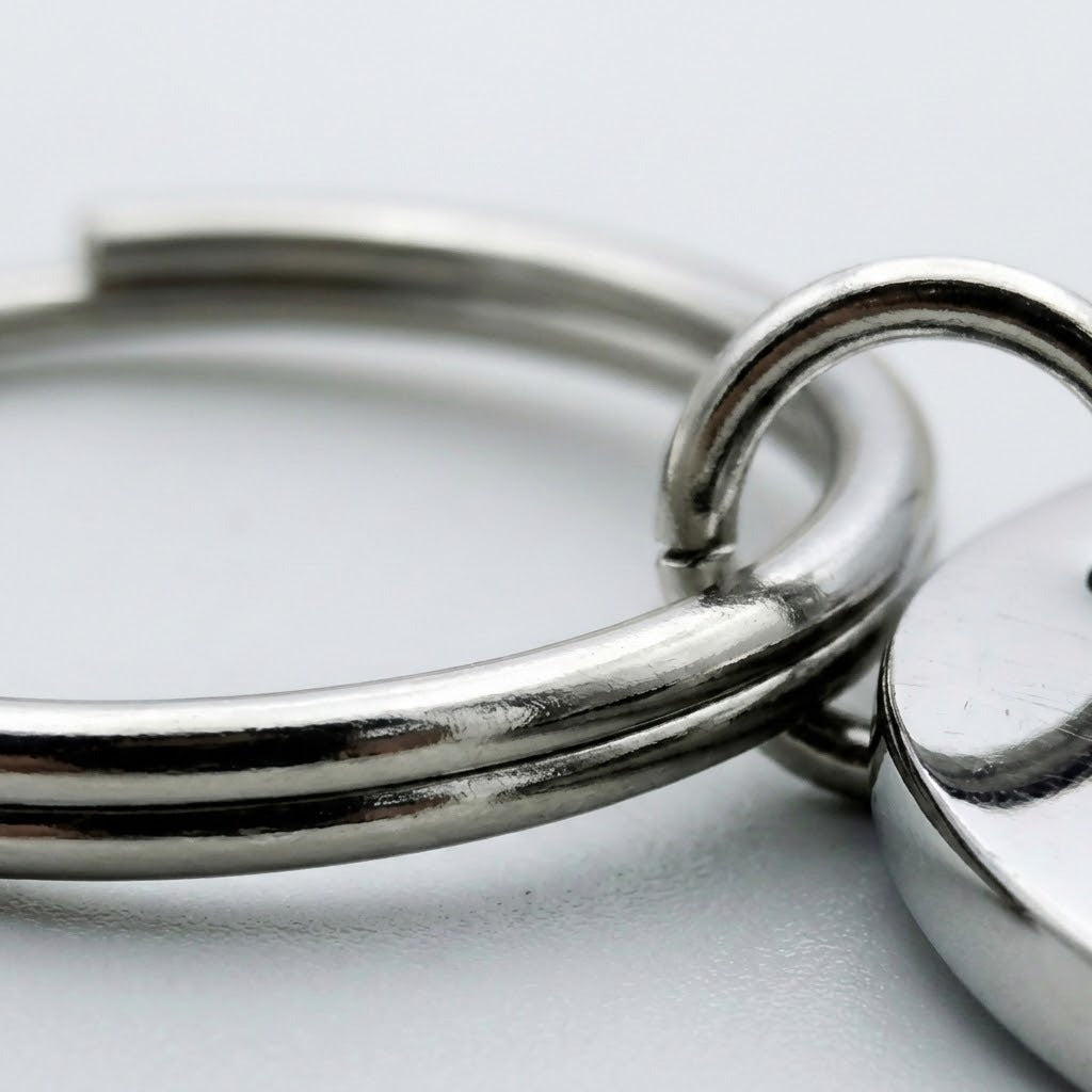Silver stainless steel keychain close-up showing the split ring, connector ring, and polished pendant edge against a pale background.