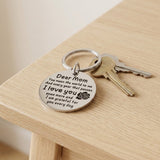 Silver Dear Mom keychain with a black rose motif rests beside two keys on a light wooden tabletop.