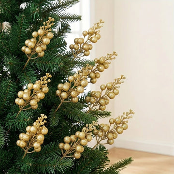Gold glitter berry picks decorate green Christmas tree branches beside a cream wall and light wooden floor.