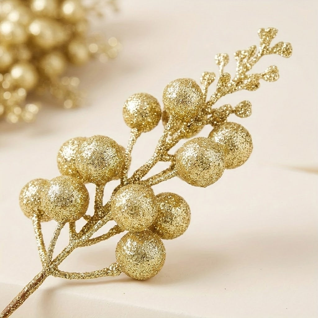 A gold glitter berry pick displays round berries and small branching tips in close-up against a softly blurred cream background.