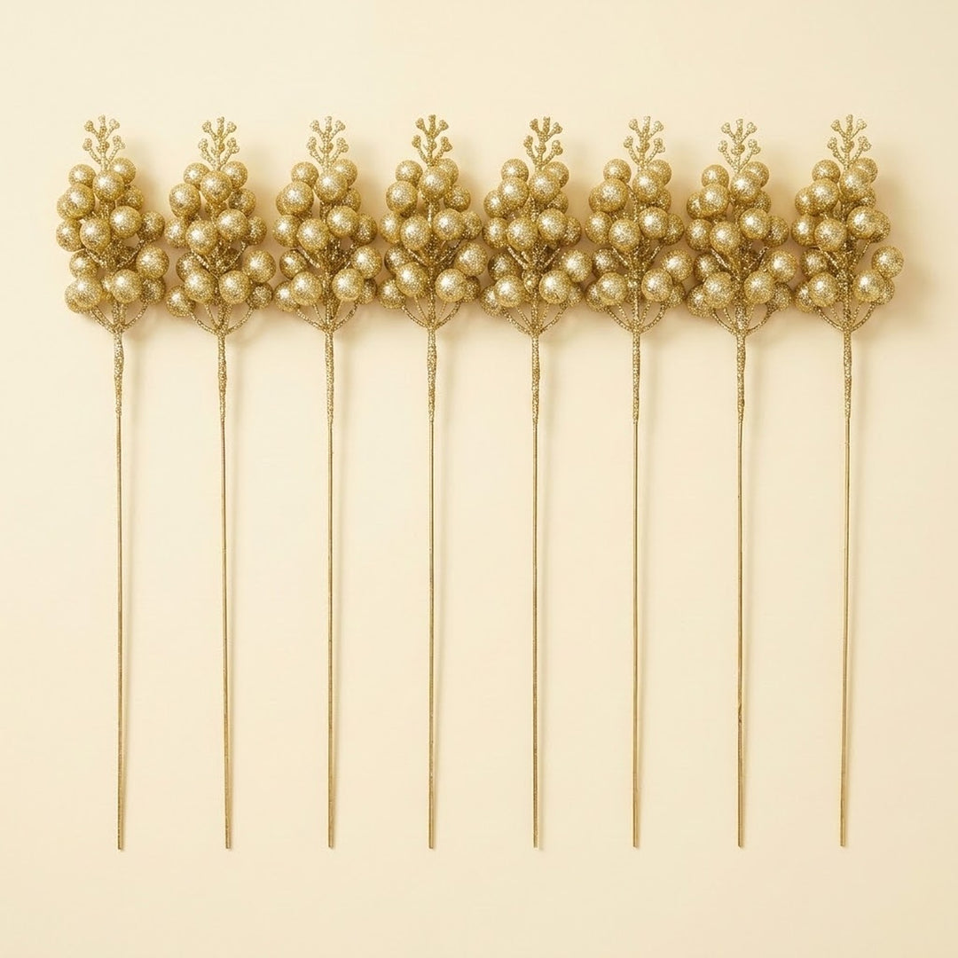 Eight gold glitter berry picks with long straight stems lie side by side on a cream background.