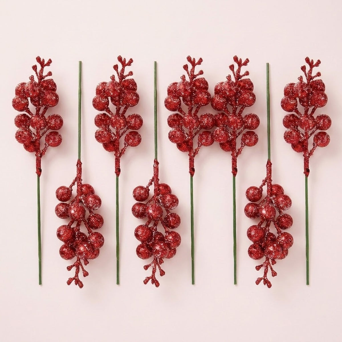 Eight red glitter berry picks with green stems alternate upright and upside down on a pale pink background.