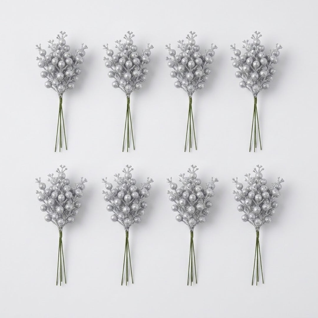 Eight bunches of silver glitter berry picks with green stems form two rows of four on a pale gray background.