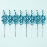 Eight turquoise blue glitter berry picks with long slender stems lie side by side on a pale blue background.