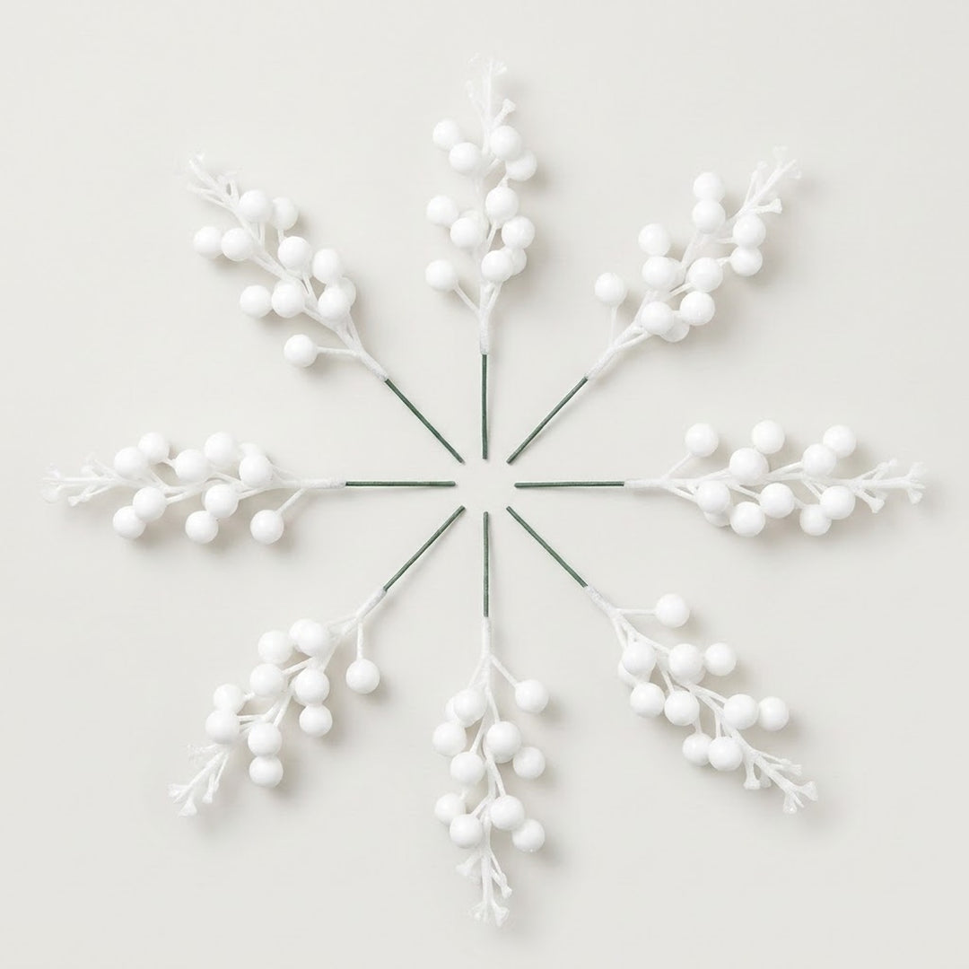 Eight matte white berry picks with green stems form a radial arrangement on an off-white background.