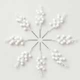 Eight matte white berry picks with green stems form a radial arrangement on an off-white background.