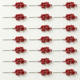 Twenty-one red glitter berry picks with green stems lie in seven rows of three on a light background.