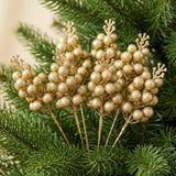 Gold glitter berry picks with round berries and branching tips nestle among dense green Christmas tree branches.