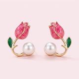 Bright pink tulip bud stud earrings with gold-tone stems, green leaves, and white pearl-like beads on a light pink background.