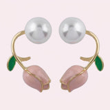 Pale pink tulip bud stud earrings with curved gold-tone stems, green leaves, and large white pearl-like beads on a pale background.
