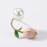 A tulip stud earring rests diagonally on white, with a gold-tone stem, green leaf, pink bud, and white pearl-like bead.