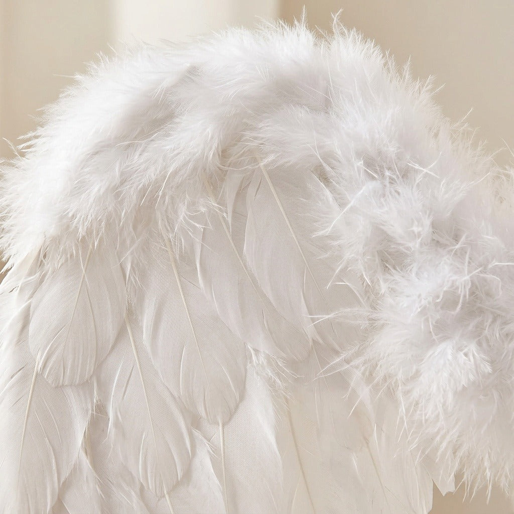 Close-up of layered white feathers and fluffy down along a costume wing against a softly blurred beige background.