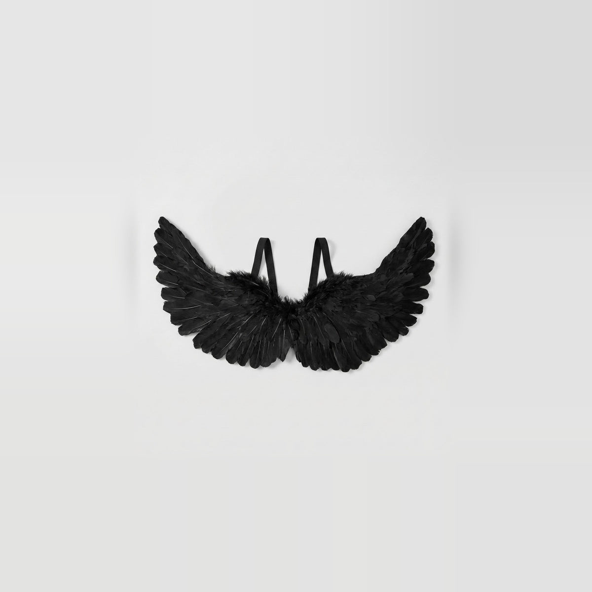 Black feather costume wings have upward-curving tips and two visible shoulder loops against a pale gray background.