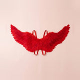 Red feather costume wings spread wide with layered feathers and matching shoulder straps against a pale peach background.