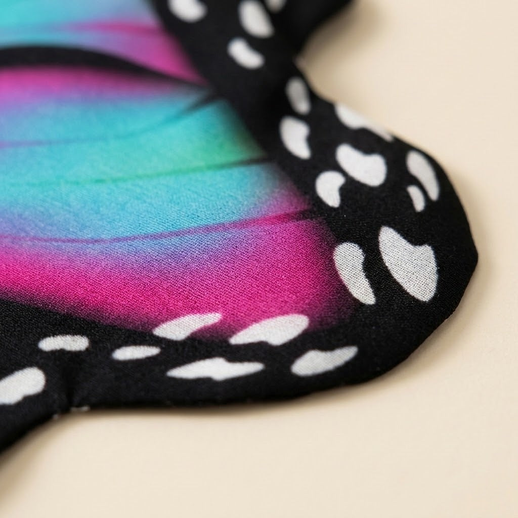 Close-up of a pink and turquoise chiffon butterfly cape shows fine fabric texture and a white-spotted black edge against a cream background.