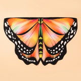 Orange and yellow butterfly wing cape with black spotted edges and a green body, laid flat on a peach background.