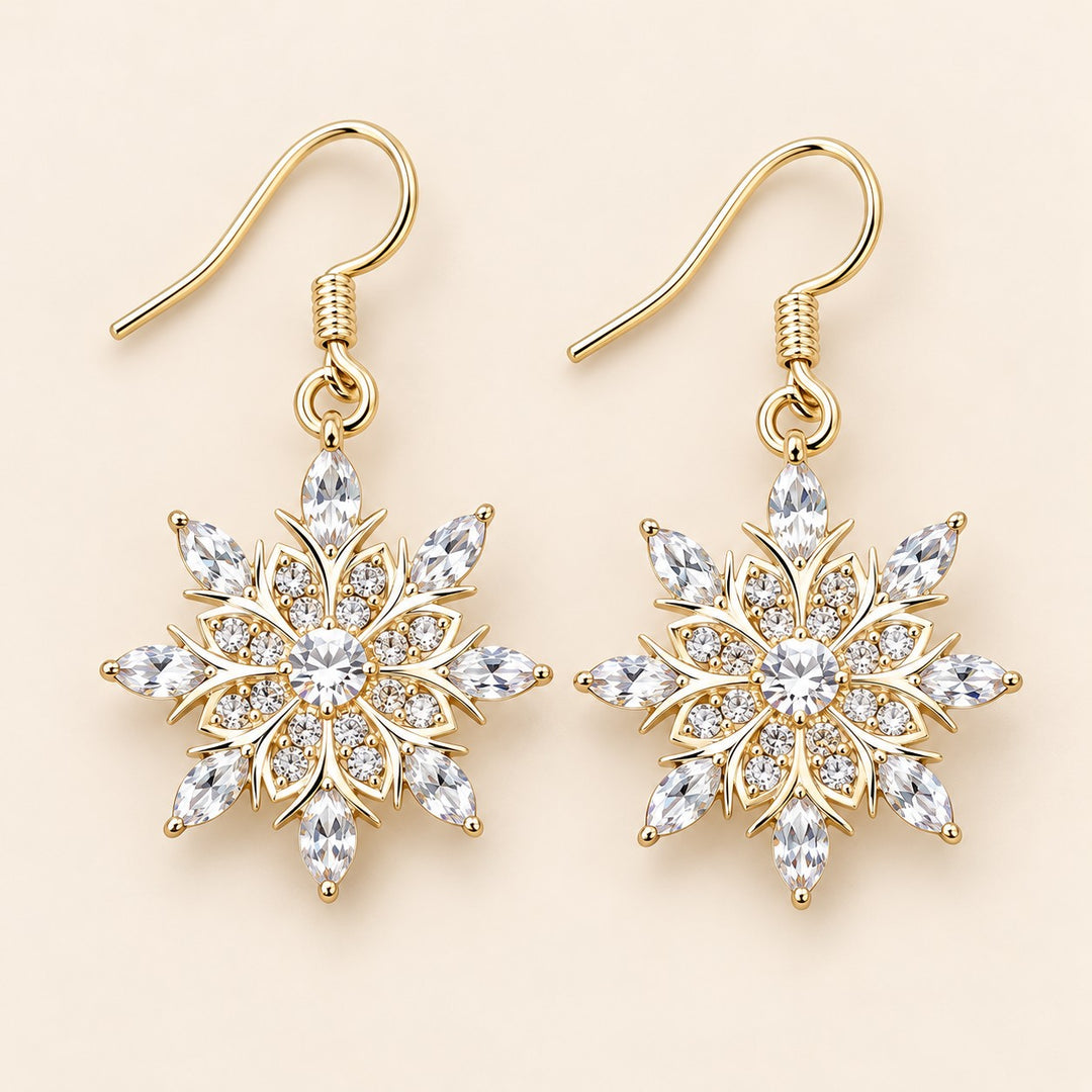 Clear crystal snowflake drop earrings with gold-tone hooks on a champagne backdrop.