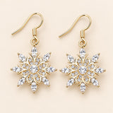 Clear crystal snowflake drop earrings with gold-tone hooks on a champagne backdrop.