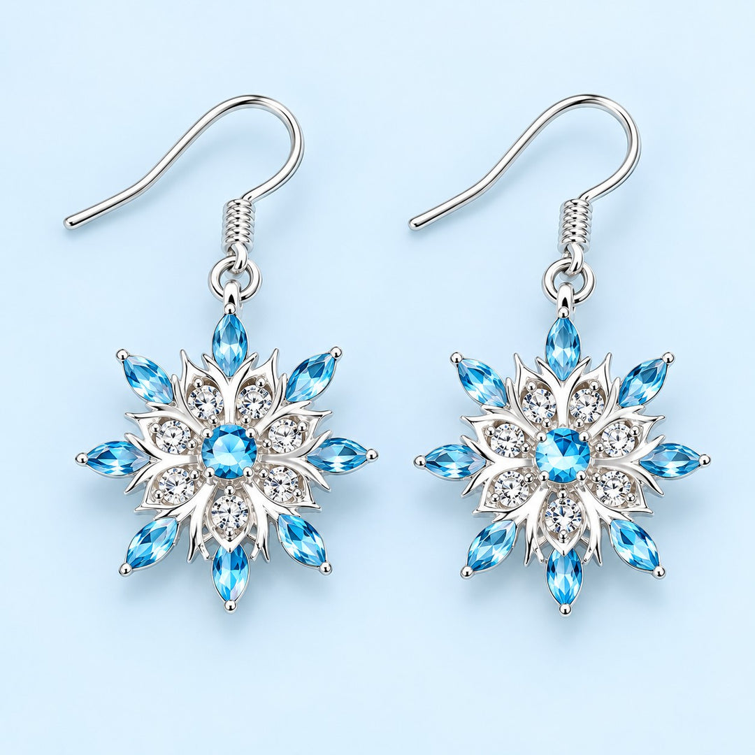 Blue and clear crystal snowflake drop earrings on a pale icy blue studio background.
