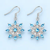 Blue and clear crystal snowflake drop earrings on a pale icy blue studio background.