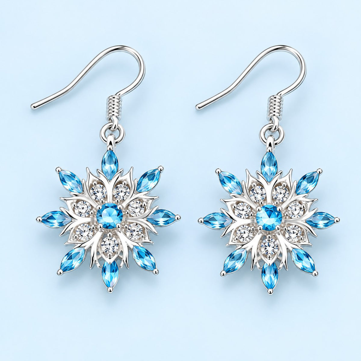 Blue and clear crystal snowflake drop earrings on a pale icy blue studio background.