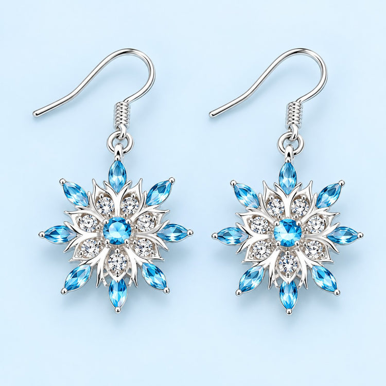 Blue and clear crystal snowflake drop earrings on a pale icy blue studio background.