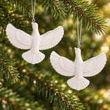 Two white acrylic dove ornaments highlight their detailed feathered wings against evergreen branches.