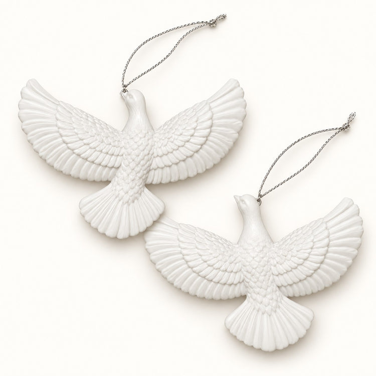 Two white acrylic dove ornaments with silver cords are centered on a soft ivory studio backdrop.