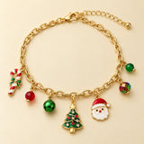 Gold Christmas charm bracelet with Santa, tree, candy cane and red-green beads on a pale cream studio backdrop.