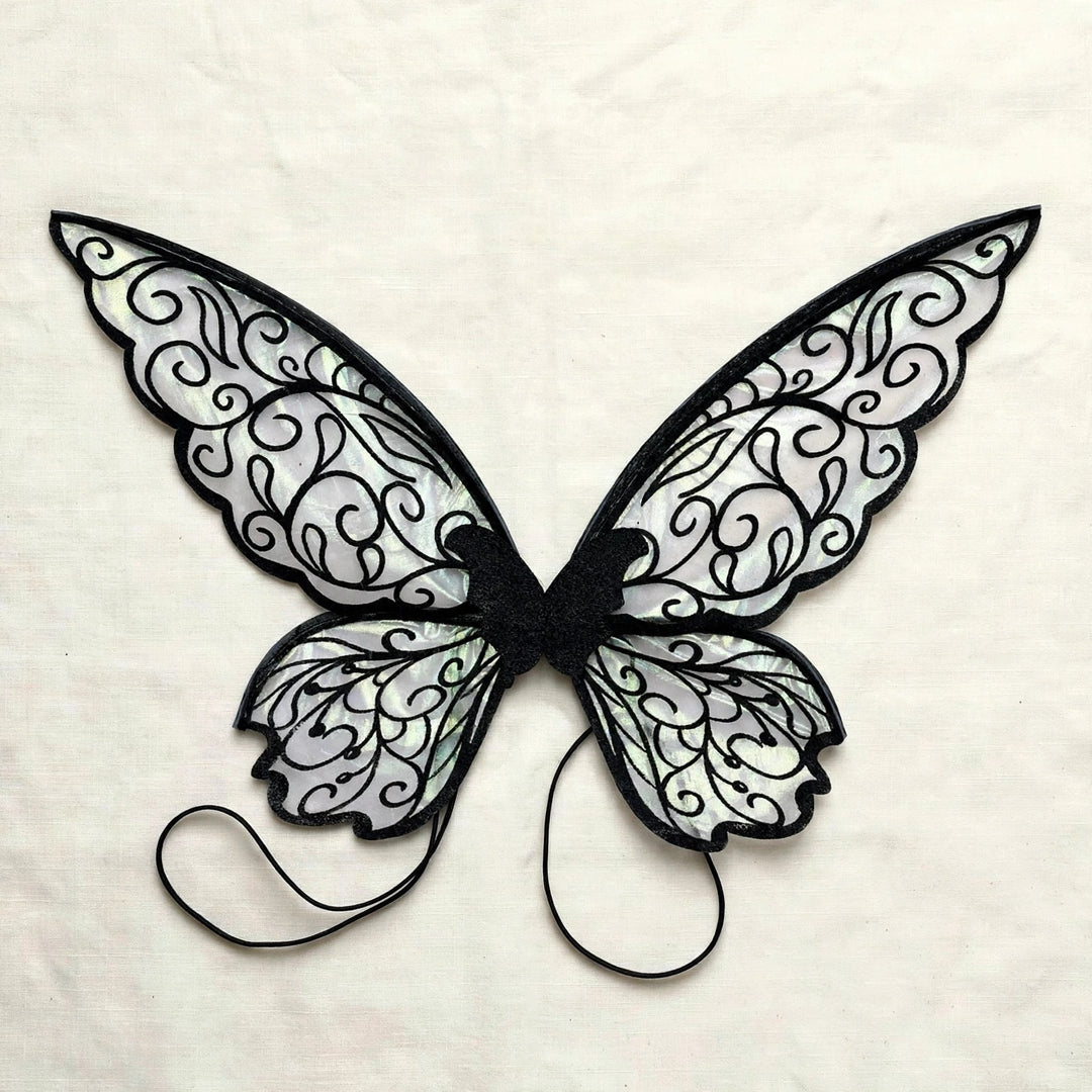 Translucent fairy wings with black swirling patterns and two black shoulder loops lie flat on cream fabric.