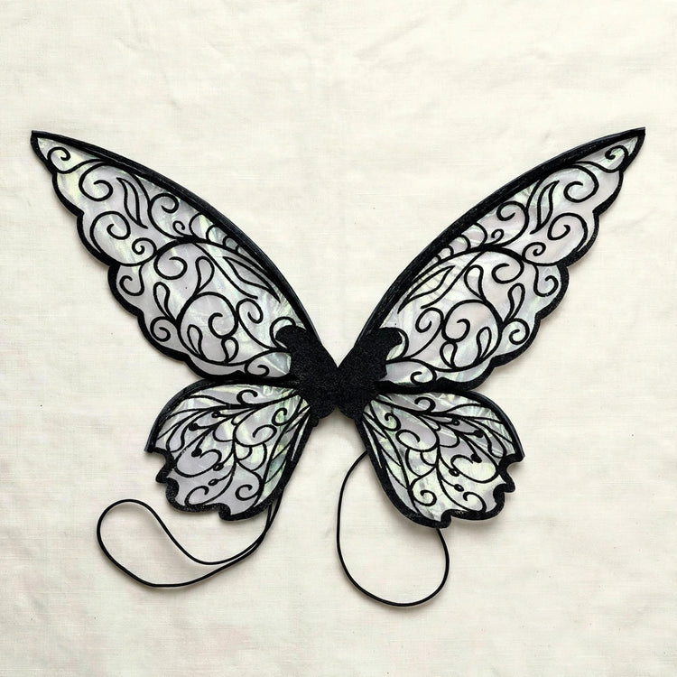 Translucent fairy wings with black swirling patterns and two black shoulder loops lie flat on cream fabric.