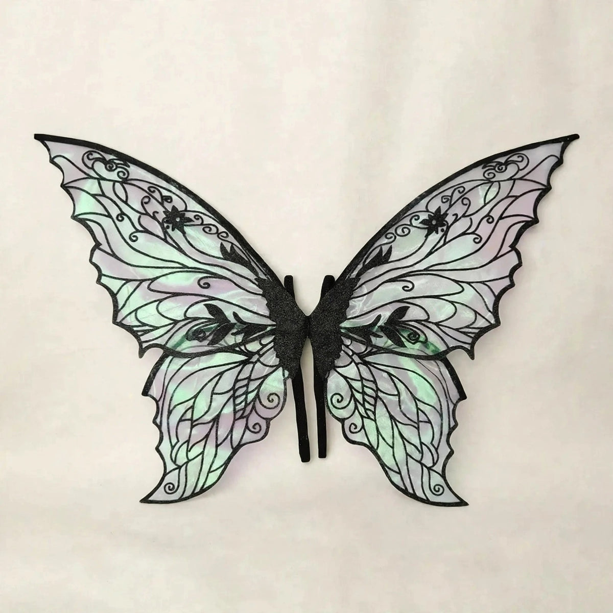Fairy wings with black floral patterns, iridescent panels, and scalloped edges spread against a cream background.