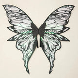 Fairy wings with black outlines, translucent green reflections, and long tapered lower tips rest against a cream background.