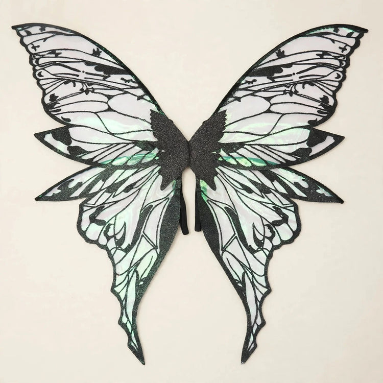 Fairy wings with black outlines, translucent green reflections, and long tapered lower tips rest against a cream background.