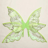 Lime green fairy wings with translucent iridescent panels, glittery swirling patterns, and pointed edges rest against a cream background.