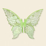 Pale green fairy wings feature translucent panels, glittery swirling patterns, scalloped edges, and central straps against a cream background.