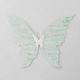 White fairy wings with translucent pale green reflections, delicate swirling patterns, and pointed lower tips rest against a light grey background.