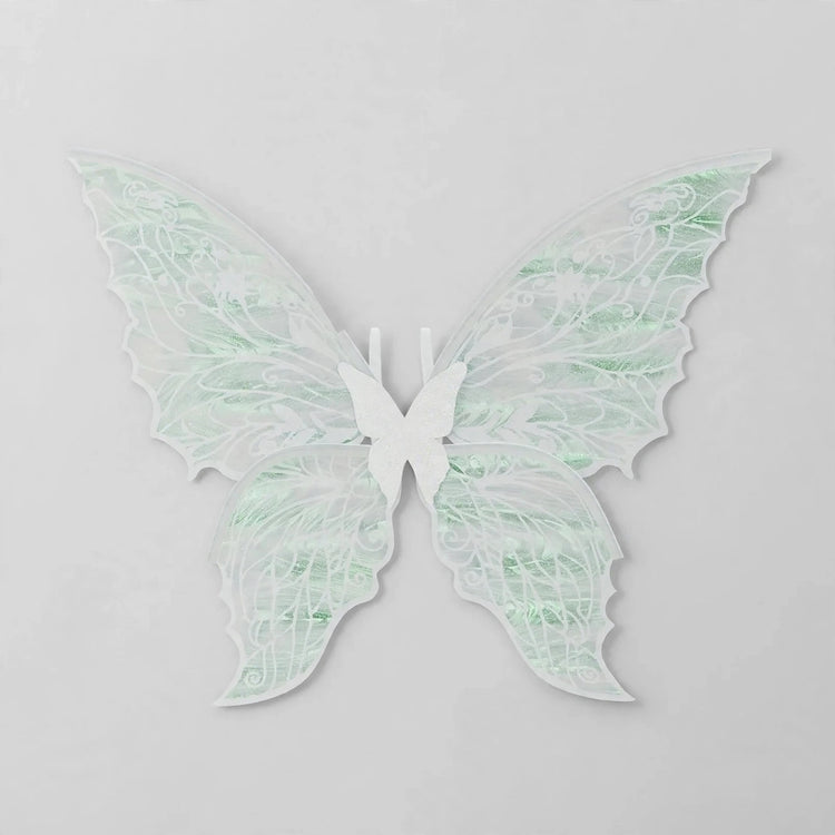 White fairy wings with translucent pale green reflections, delicate swirling patterns, and pointed lower tips rest against a light grey background.