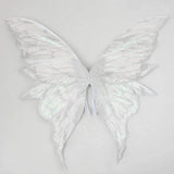 White iridescent fairy wings with glittery vein patterns and long curved lower tips spread against a light grey background.