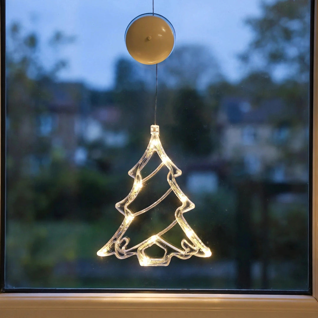 Transparent Christmas tree-shaped lighted ornament with warm white LED lights hangs on a window at dusk, beneath a round cream suction cup.