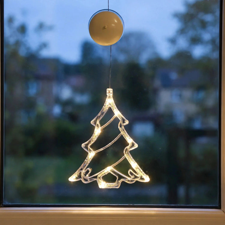Transparent Christmas tree-shaped lighted ornament with warm white LED lights hangs on a window at dusk, beneath a round cream suction cup.