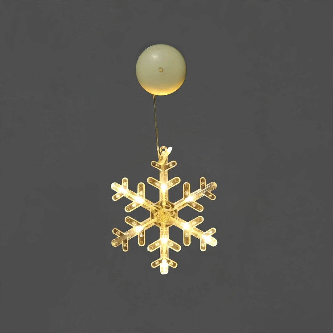 Clear snowflake-shaped lighted ornament with warm white lights hangs beneath a round cream suction cup against a plain gray background.