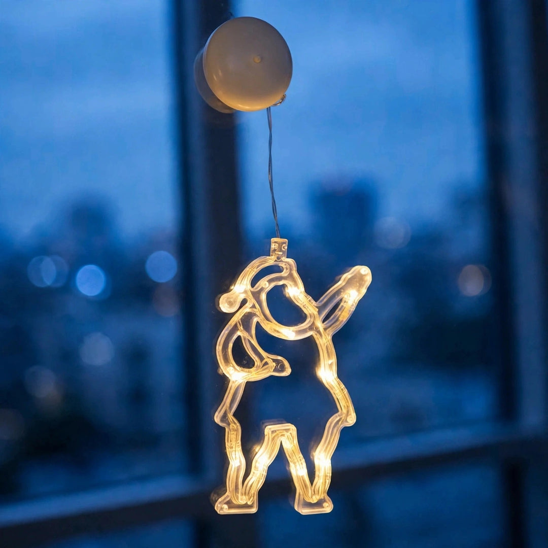 Clear Santa-shaped lighted ornament glows with warm white lights on a window against a blurred blue evening cityscape.