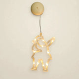 A clear Santa-shaped lighted ornament with one raised arm glows warm yellow beneath a round beige housing against an off-white background.