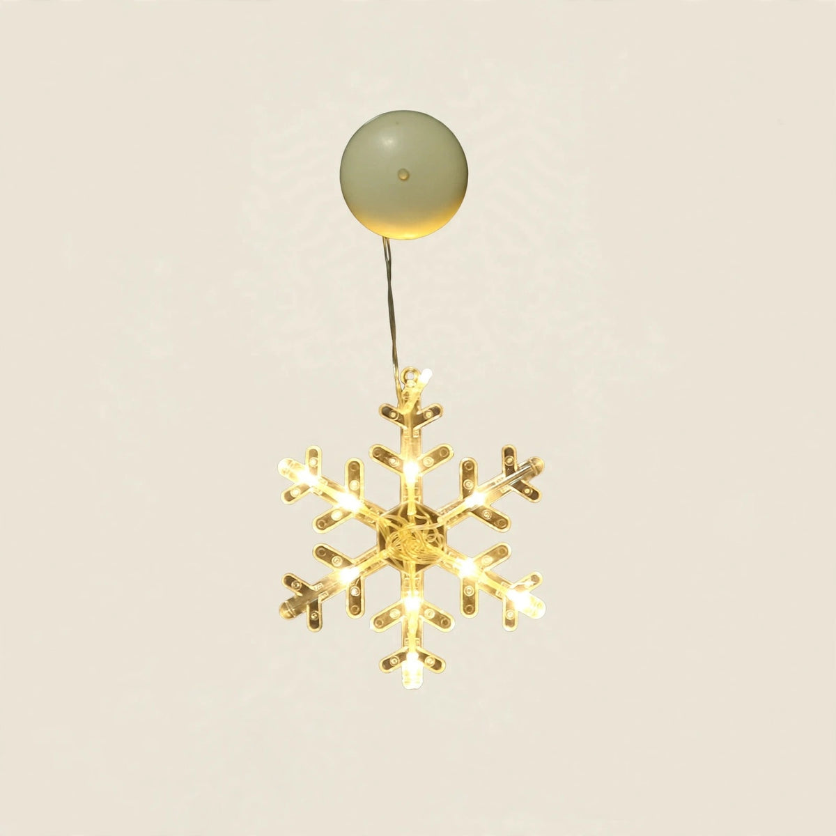 A clear six-pointed snowflake-shaped lighted ornament glows warm yellow beneath a round cream housing against an off-white background.