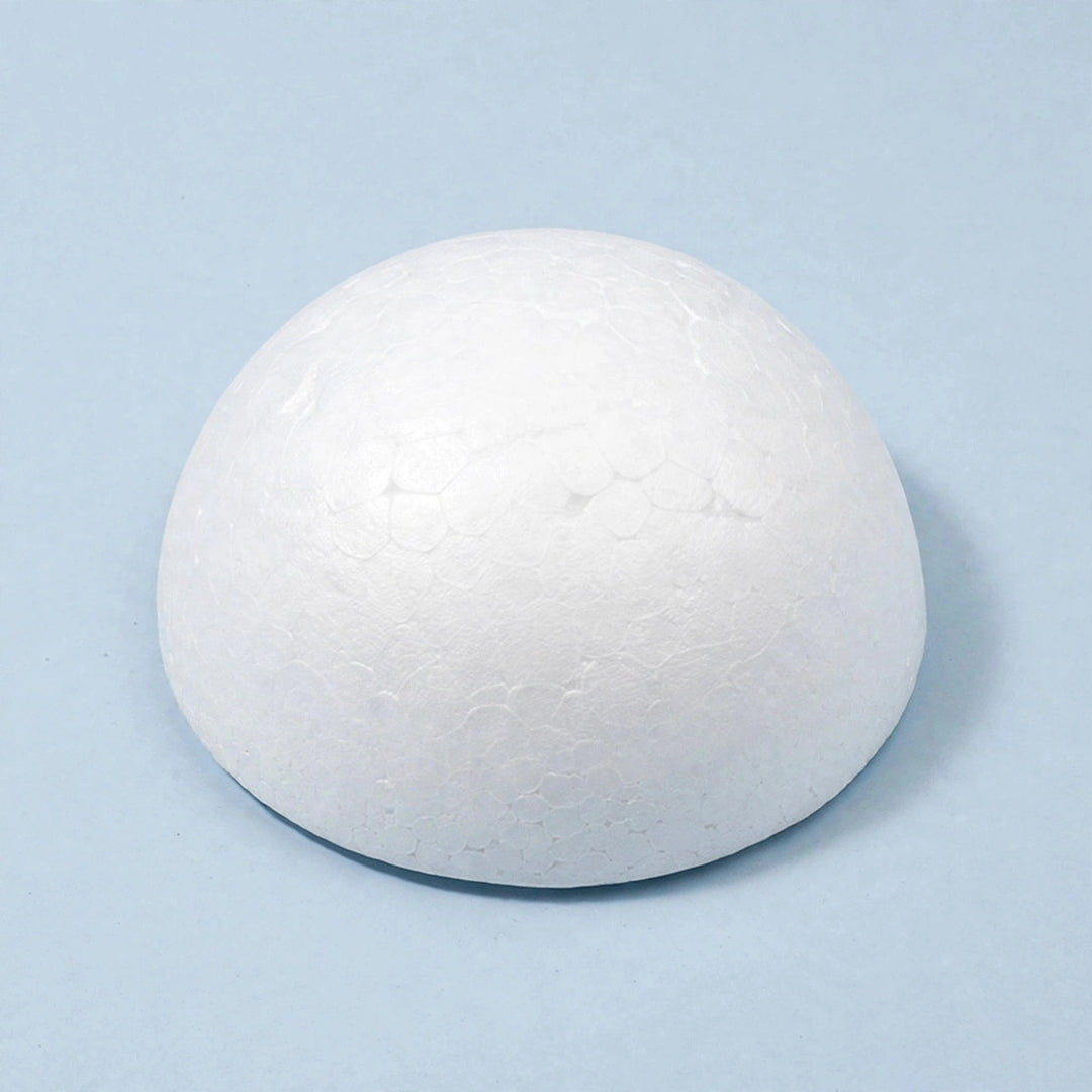 A white polystyrene foam half ball rests on a pale blue surface against a matching background, casting a shadow to the right.