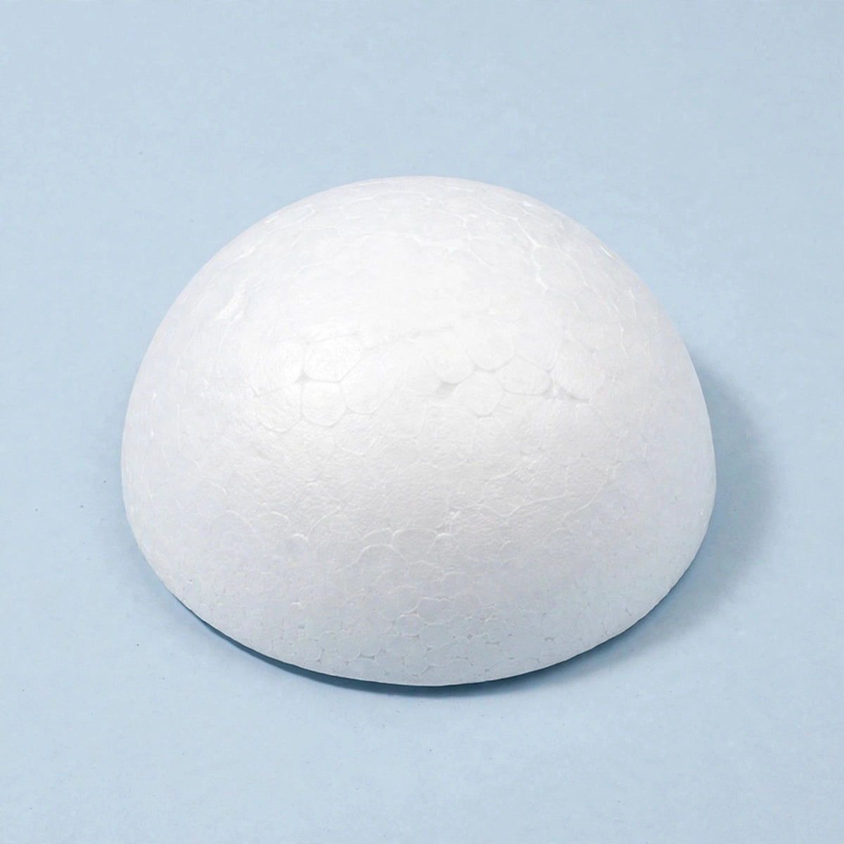 A white polystyrene foam half ball rests on a pale blue surface against a matching background, casting a shadow to the right.