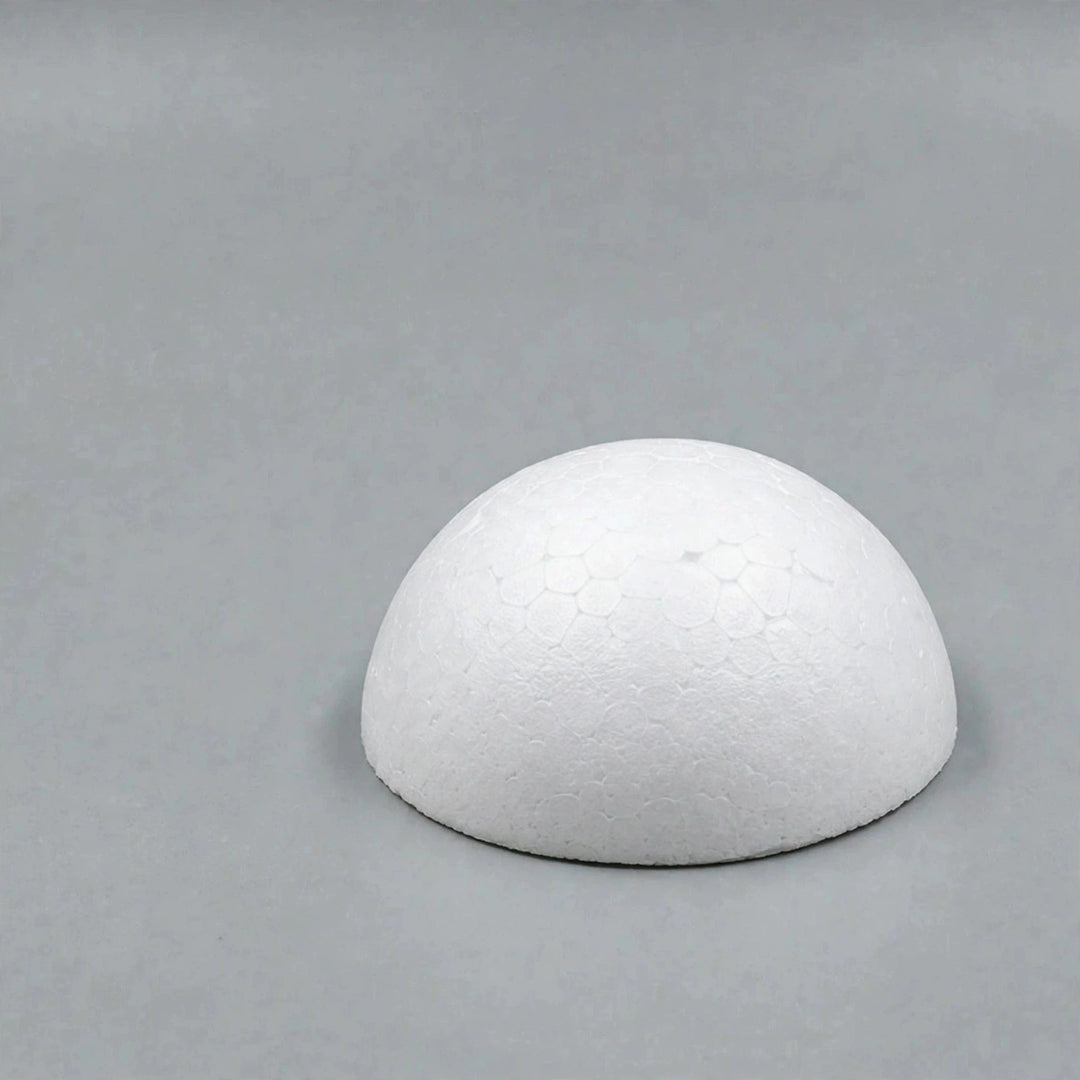 A white foam half ball with a lightly textured surface sits on its flat base against a plain gray background.