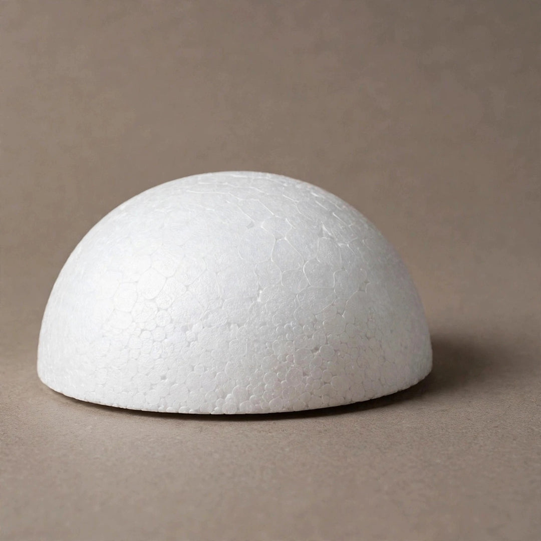A white polystyrene foam half ball sits on a taupe surface against a matching background, casting a shadow to the right.