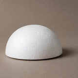 A white polystyrene foam half ball sits on a taupe surface against a matching background, casting a shadow to the right.